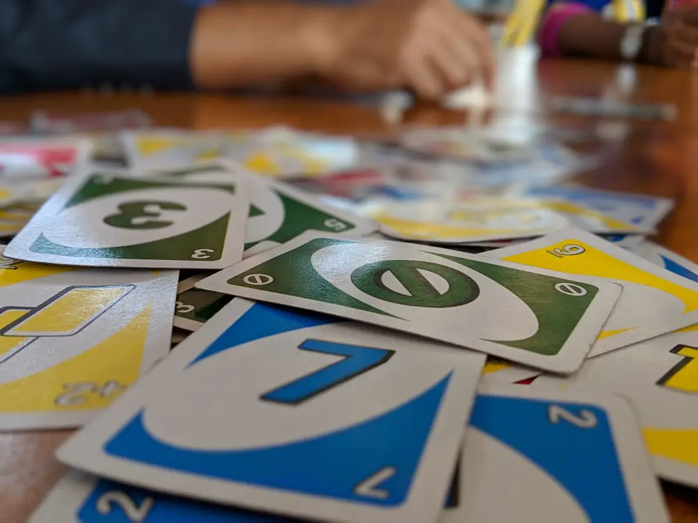 Scattered collection of Uno cards on a table while some people play in the background.