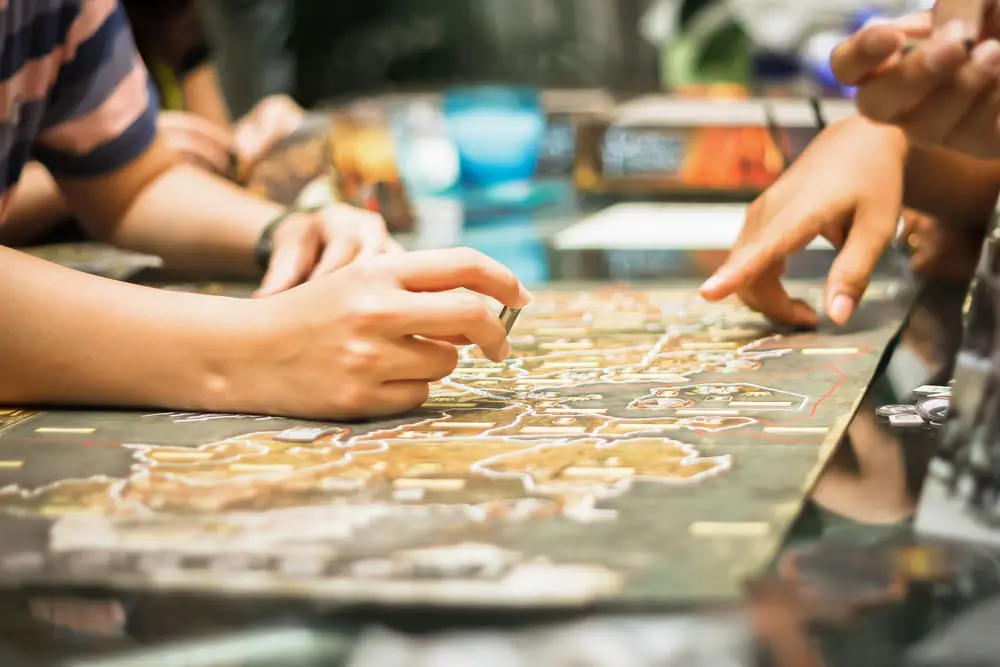 Closeup of someone pointing at a spot on a board game and someone else thinking about what to do.