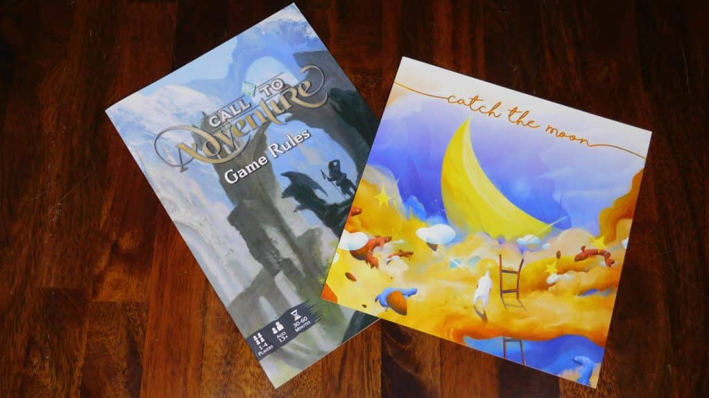 A closeup of the rulebooks for Call To Adventure and Catch The Moon.