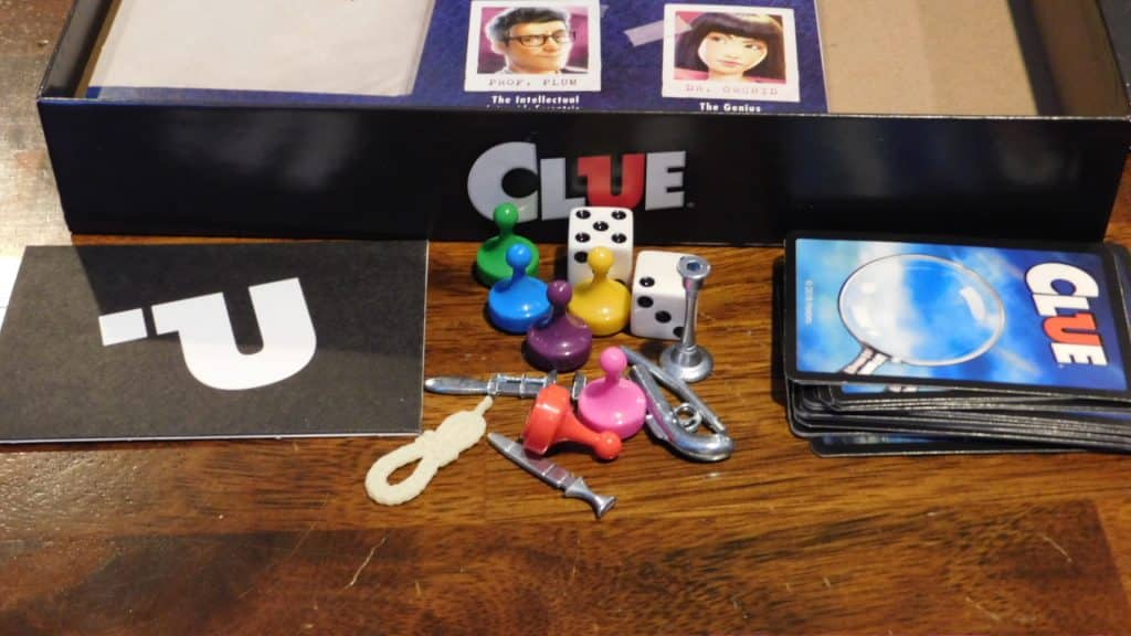 A closeup of the components of Clue (2018) along with the game box.