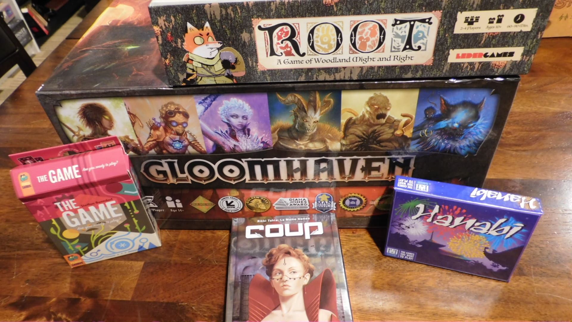 Some games on a table, including The Game, Coup, Hanabi, Root, and Gloomhaven.
