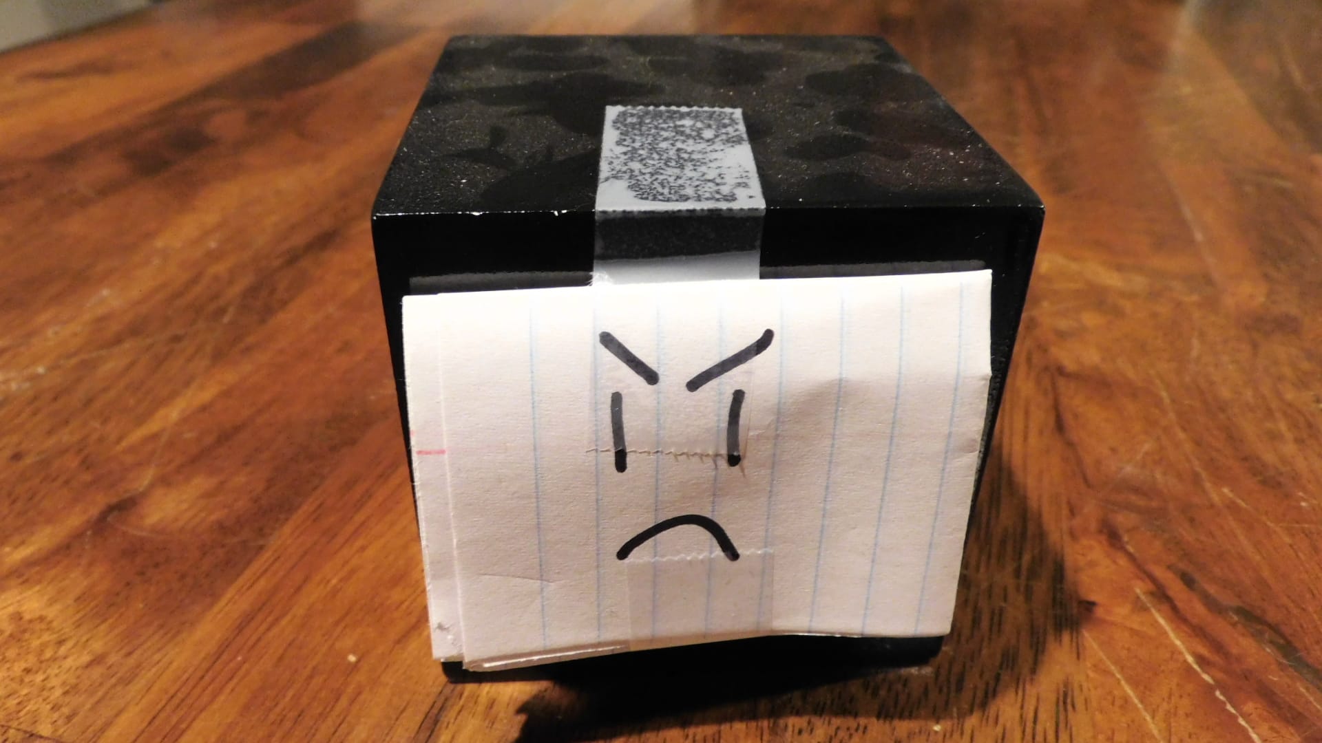 A black cube with a piece of paper on it with a face on the paper.