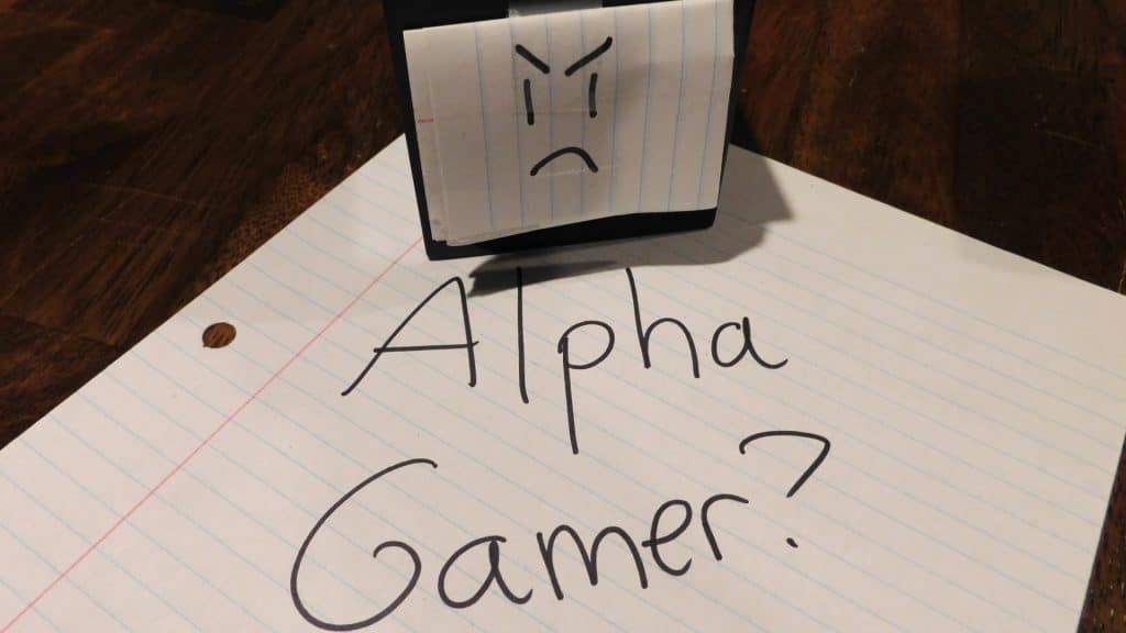 A piece of paper that says, "Alpha Gamer?" along with a black cube with a face on it on a piece of paper.