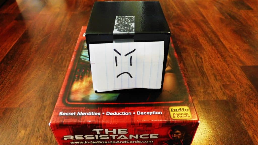 A closeup of Alpha Gamer Al sitting on type of the game box for The Resistance.