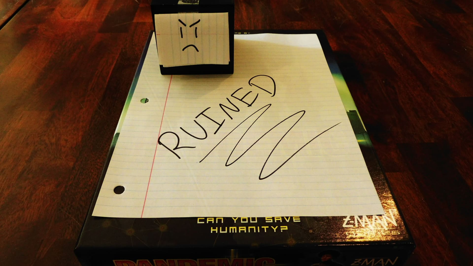 Alpha Gamer Al sitting on a piece of paper that says "Ruined," which is on top of a board game.