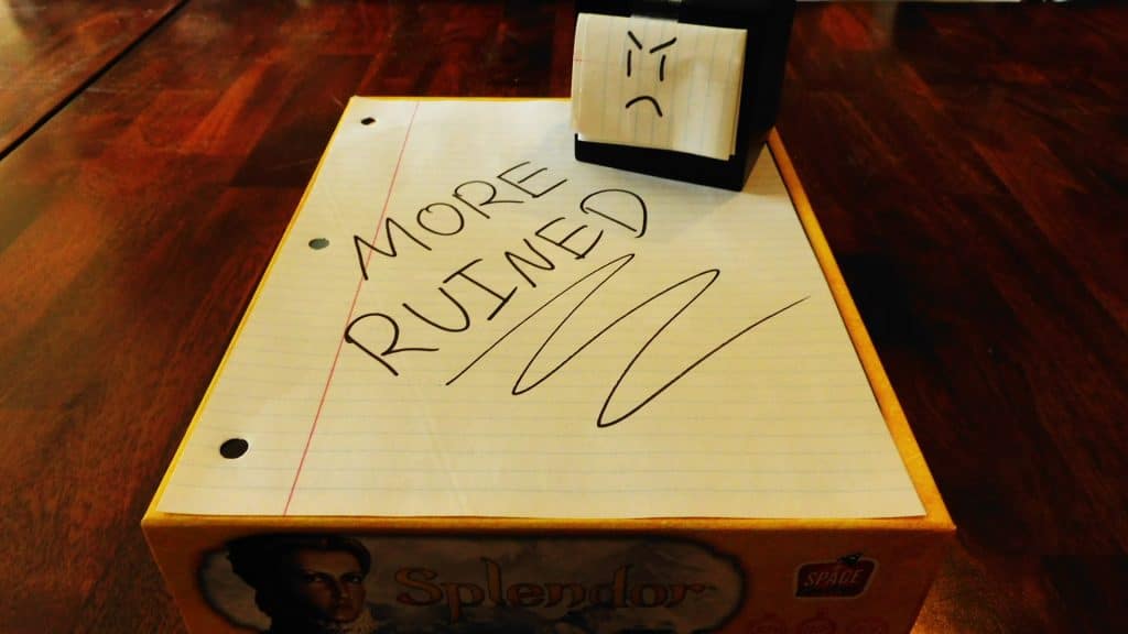 Alpha Gamer Al sitting on top of a piece of paper that says, "MORE RUINED," which is on top of a board game.