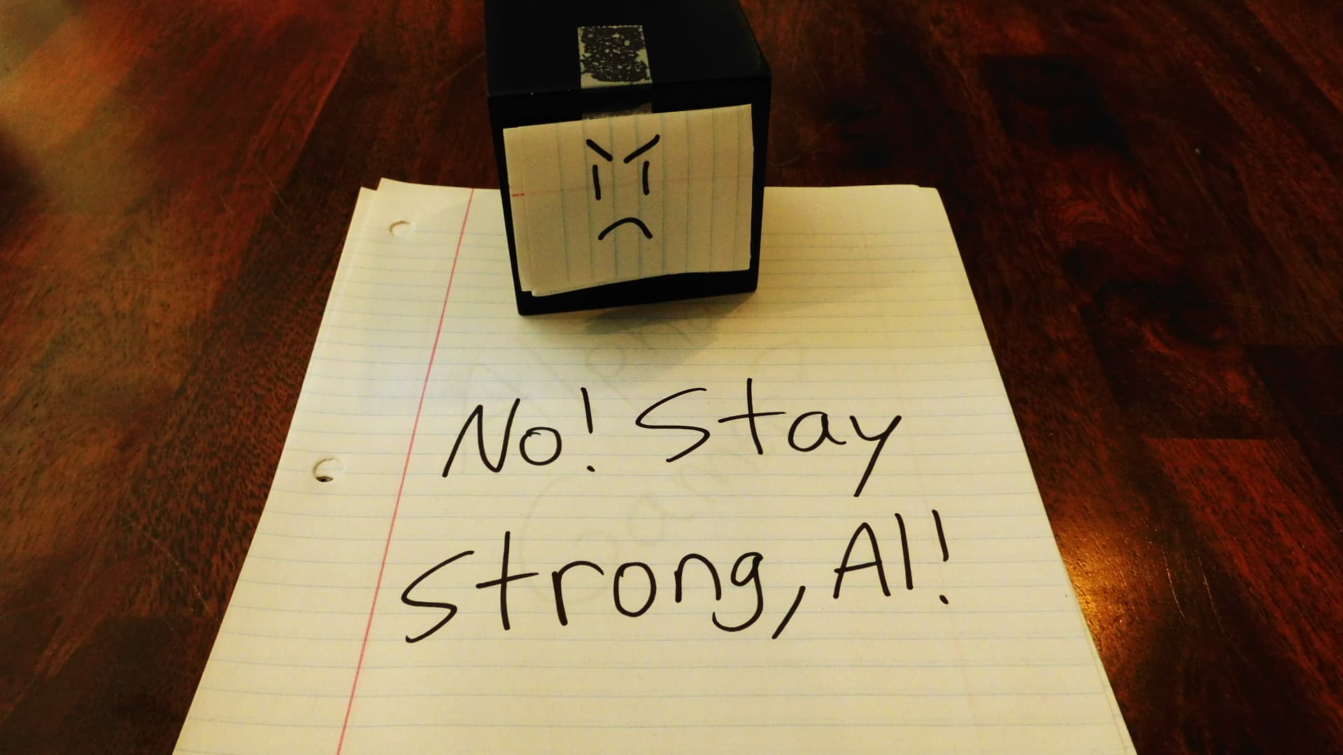 Alpha Gamer Al sitting on a piece of paper that says, "No! Stay Strong, Al!"