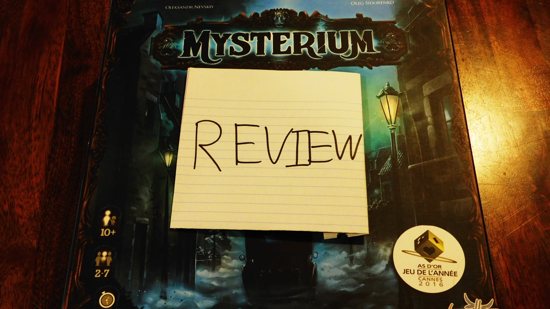 The game box for Mysterium with a piece of paper on it saying Review.