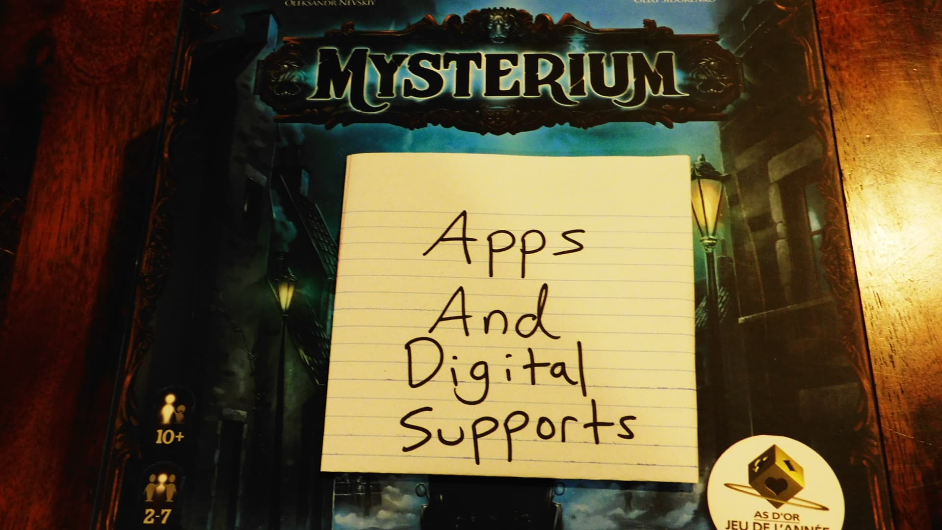 Mysterium's game box with a piece of paper on it reading "Apps And Digital Supports."